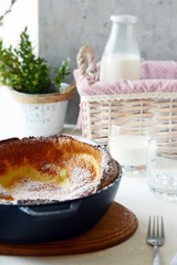 Fresh homemade dutch baby pancake with powdered sugar, fresh berries and mint for breakfast with a glass of milk and apple juice on a light background. Delicious sweet breakfast in a sunny interior. 