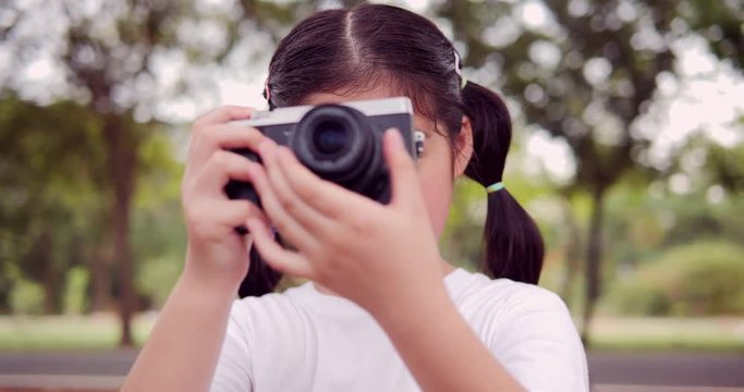 Asian little girl using vintage camera at outdoor park with happy emotion.