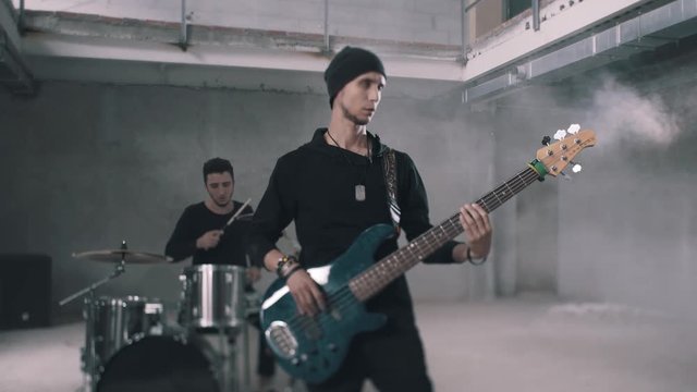Drummer and bass guitarist playing instruments in a smoky room. Rock band. Average plan. Beautiful picture.