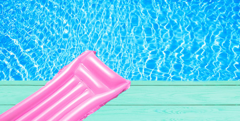 Beach summer holiday background. Inflatable air mattress on swimming pool water. Pink lilo and summertime accessories on poolside wooden floor. Top view and copy space. Banner