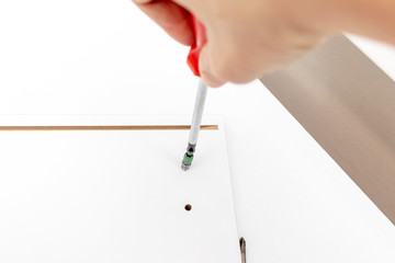 Assembling white furniture, she tighten a screw with a screwdriver, close up view