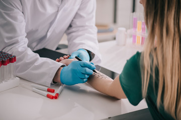 cropped view of doctor in white coat and latex gloves holding marker pen near marked female hand