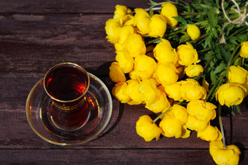 a bouquet of yellow buttercups and a transparent Cup of tea on a background of wooden boards