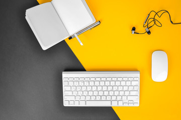 Office workplace minimal concept. Computer keyboard with blank notebook, pen, headphones on black & yellow background. Top view with copy space, flat lay.