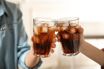 Women holding glasses of cola with ice on blurred background, closeup