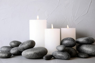 Fototapeta na wymiar Zen stones and lighted candles on table against light background