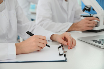 Medical student with clipboard working in scientific laboratory, closeup
