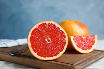 Fresh tasty grapefruits on board against color background