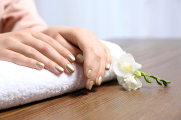 Obraz na płótnie Canvas Woman with gold manicure on rolled towel at table, closeup. Nail polish trends