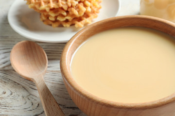Bowl with condensed milk served on table, closeup. Dairy products
