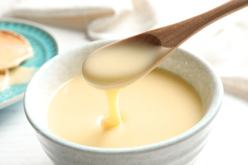 Spoon of pouring condensed milk over bowl on table, closeup. Dairy products