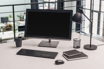 modern workplace with computer, coffee to go, lamp and stationery in office
