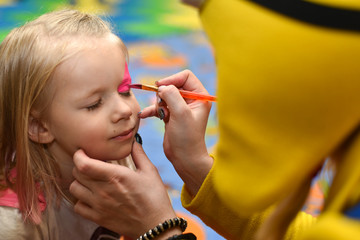 Animator paints the face of a little girl paint on a holiday