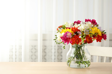 Vase with bouquet of spring freesia flowers on table in room