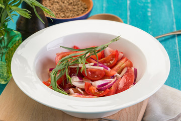 Delicious summer salad with fresh tomatoes and red onions, decorated with a sprig of tarragon, on a blue wooden background