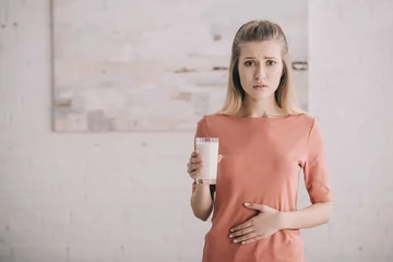 Fotobehang upset woman with lactose intolerance holding glass of milk © LIGHTFIELD STUDIOS