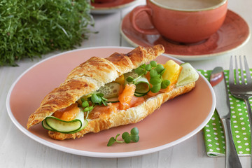 Fresh croissant with salmon slices, fresh cucumber and microgreens for breakfast