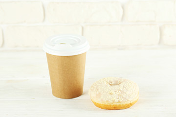 Vibrant composition of lush donut with colorful sprinkled icing and disposable paper cup on wood textured background copy space for text. Tasty but unhealthy food concept. Close up, flat lay, top view