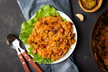 Traditional dish of polish cuisine - Bigos from fresh cabbage, meat and prunes. Top view. Dark background.