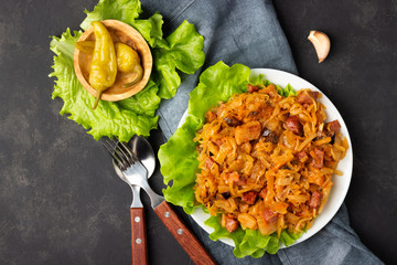 Traditional dish of polish cuisine - Bigos from fresh cabbage, meat and prunes. Top view. Dark background.