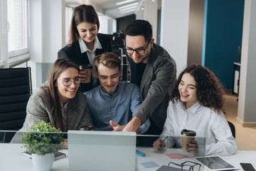 We have great results! Young man pointing at laptop with smile while sitting on the couch at office with her coworkers.