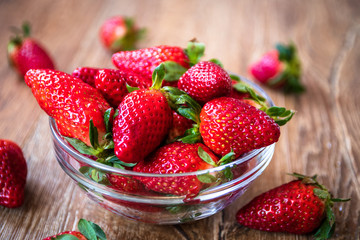 Fresh organic strawberries in a glass bowl on wooden table