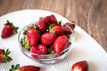 Fresh organic strawberries in a glass bowl on wooden table