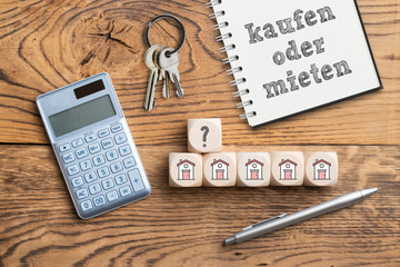 Notizblock mit Aufschrift "kaufen oder mieten?" und Taschenrechner auf Holzuntergrund 