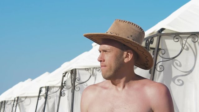 A man on vacation. A man with a hat on the beach.
