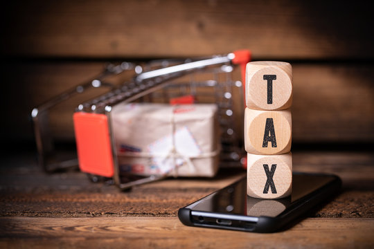 shopping cart and cubes with the word "tax" on a smartphone on wooden background