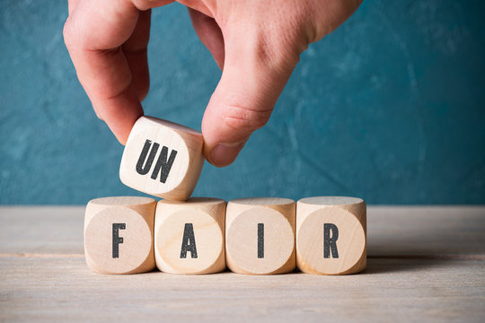 Hand verändert Wort "unfair" zu "fair" durch Wegnahme eines Würfels