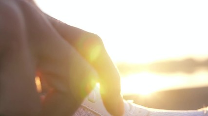 Hands tying shoelace on running shoes before jogging on the background of the sunset. Close up on running shoes. Slow motion.