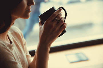 Beautiful caucasian woman sitting at a wooden table in a cafe, browsing internet using phone. and drinking coffee.
