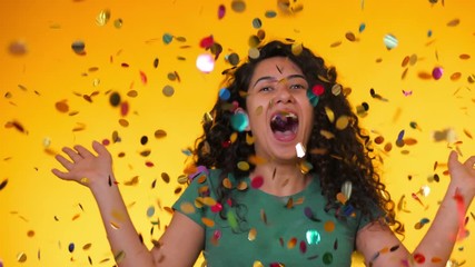 Excited latin attractive woman dancing, having fun, rejoices over confetti rain in yellow studio. Concept of happiness, party, winning