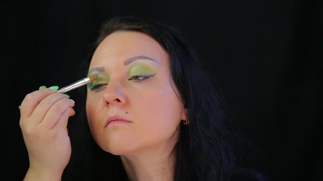 Brunette woman applies juicy green sparkles on eyelids. The average plan
