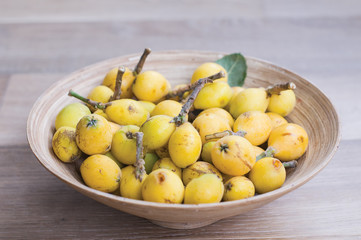 The vertical photo of Japanese fruit, loquat, in a bowl on the wooden background