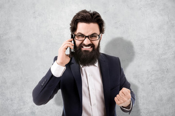 aggressive bearded businessman swears on the smartphone, image on the background a concrete wall