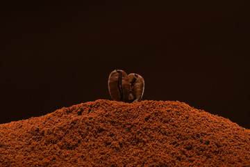 Two resh roasted coffee beans stand on a handful of ground coffee on a brown background. Isolated macro. Post card, banner. Copy space.