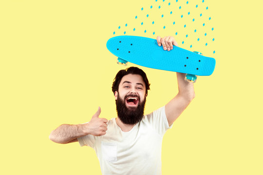 cheerful hipster man holds skateboard and shows like, concept of summer mood, image on a yellow background