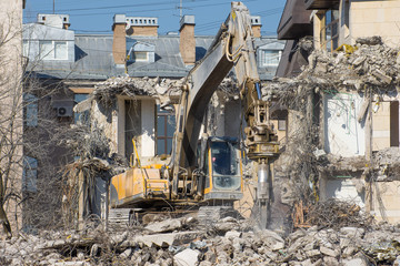 Excavator with hydraulic shears against the background of a demolished building. Dismantling of emergency construction.