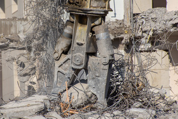 Hydraulic shears of heavy machinery on the background of the destroyed building, the collapse of metal fittings.