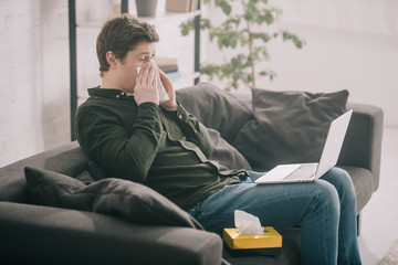 sick man having allergy and sneezing in tissue while using laptop