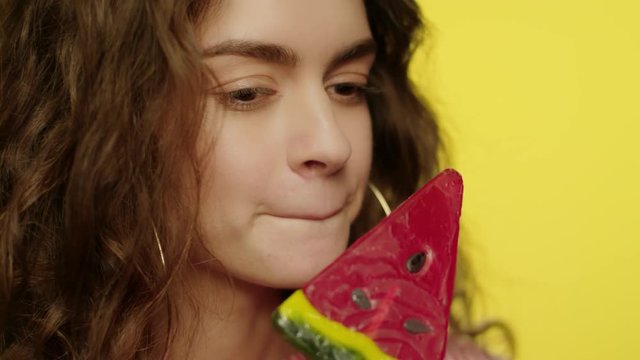 Young woman licking candy in studio. Fashion model face smiling in camera
