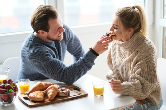 Happy young couple spending nice time together, hugging and kisses each other. Eating breakfast at home