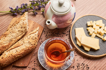 Cup of tea with cheese and bread next to a teapot