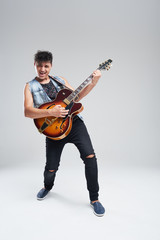 Young man musician with an electric guitar in hand on a gray background. he plays rock and roll loudly. Full-length portrait.