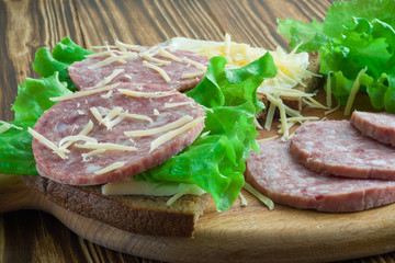 sandwiches of bread and butter, lettuce and salami sausages sprinkled with grated cheese on a cutting board and on a wooden background. angle view. close-up