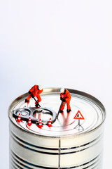 Conceptual diorama image of miniature figures trying to prise open a tin can