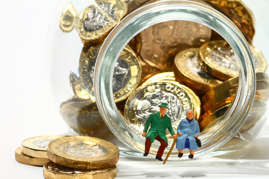 Conceptual diorama image of elderly miniature figures sat on the rim of a glass jar full of pound coins