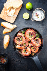 Traditional Spanish octopus braised cooked with aioli and baguette in wine sauce as top view in a cast-iron saucepan
